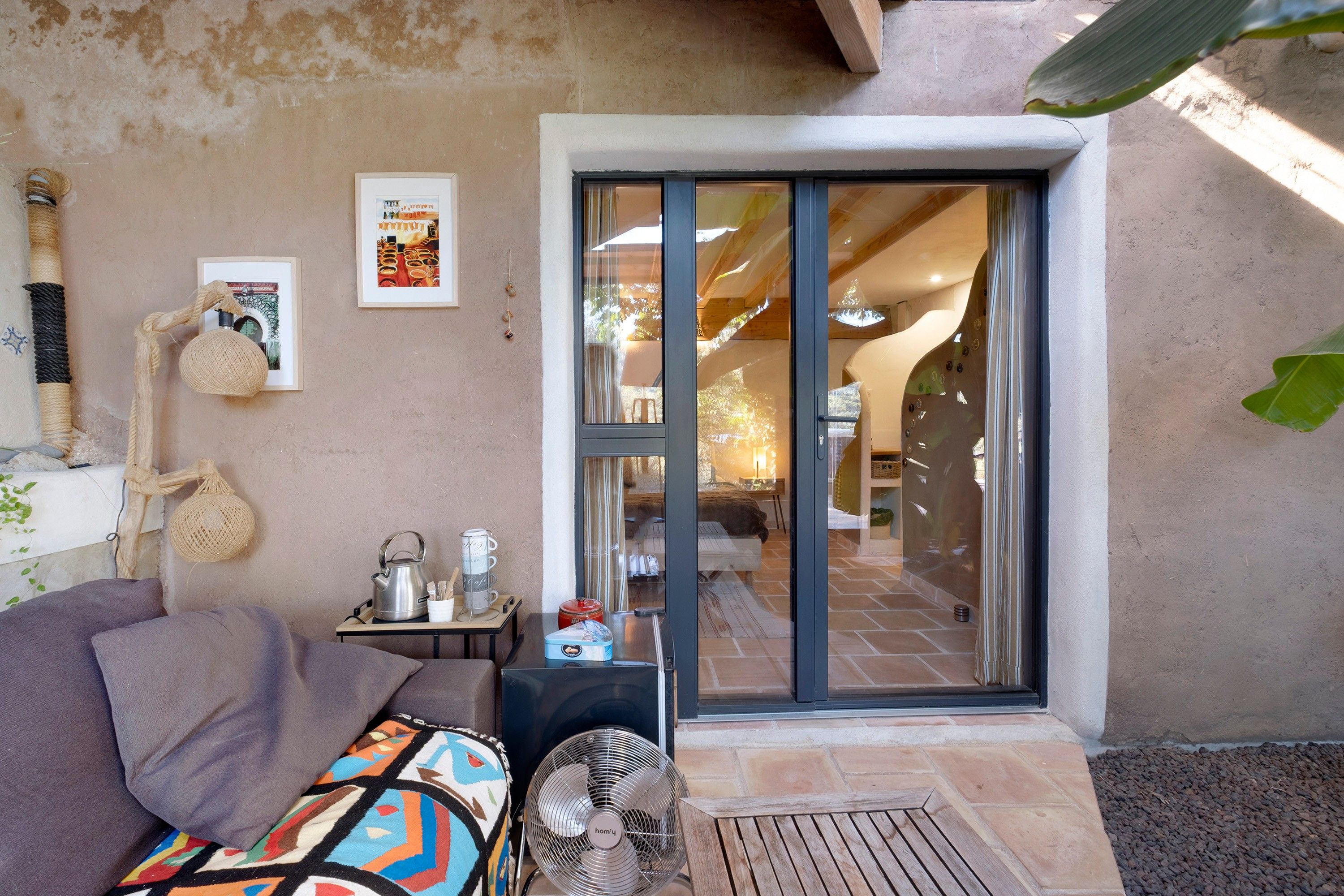 A cozy room with a sofa, a small table with a kettle, and a fan.