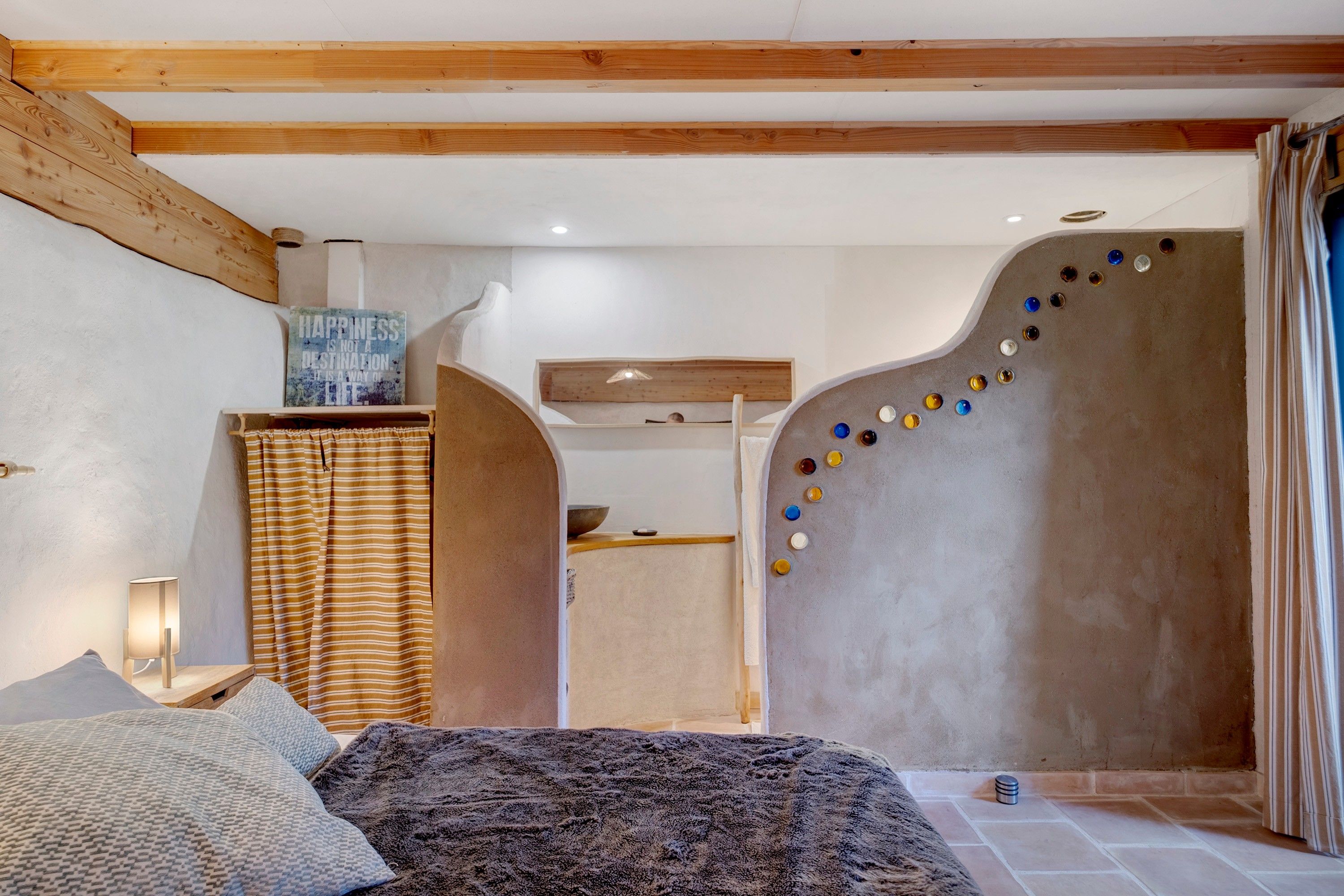 Ein Schlafzimmer mit einem Bett, einer an der Wand befestigten Ablage, einem dekorativen Wandbild und einer Wandgestaltung mit farbigen Objekten.
