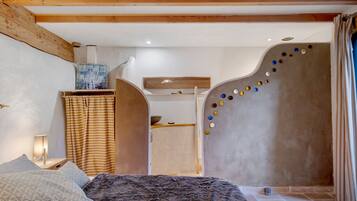 Ein Schlafzimmer mit einem Bett, einer an der Wand befestigten Ablage, einem dekorativen Wandbild und einer Wandgestaltung mit farbigen Objekten.