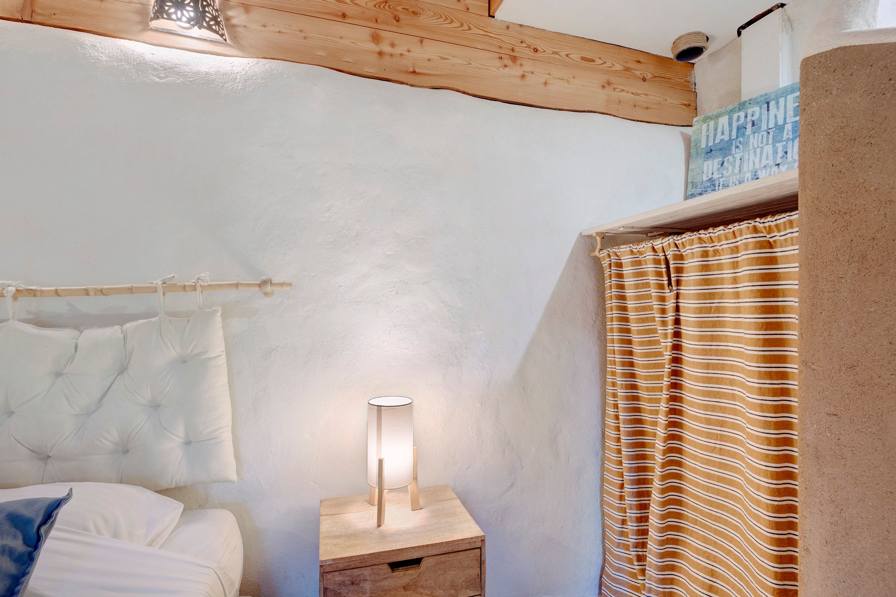 Une chambre à coucher avec un lit, une table de chevet avec une lampe, une tête de lit en bois et un rideau à rayures.