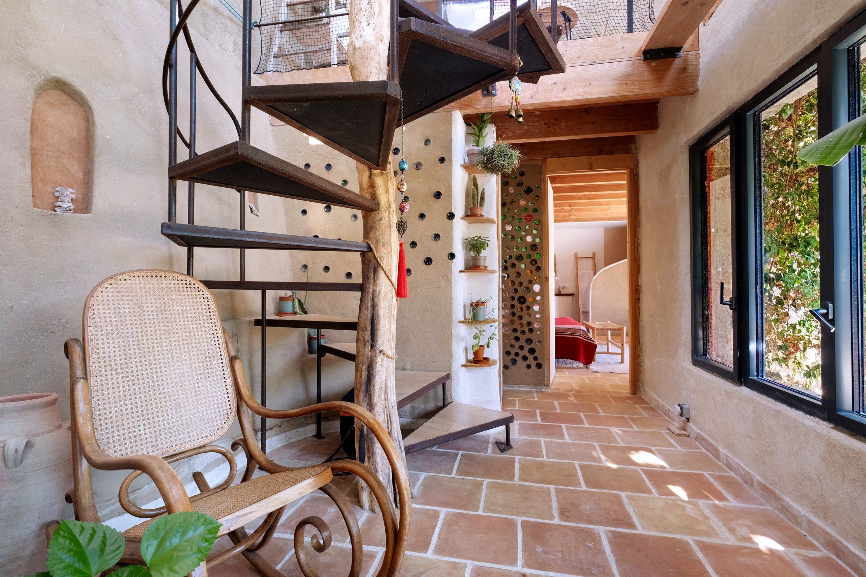 Un intérieur rustique avec une chaise en bois, un escalier en colimaçon et une vue par la fenêtre.