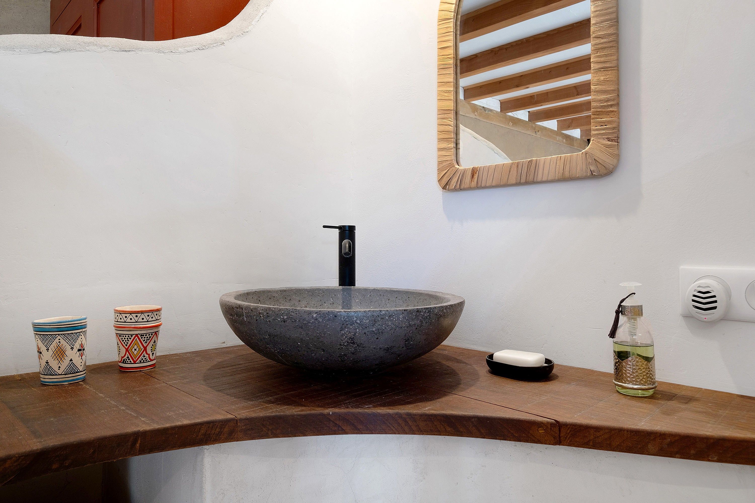 Une salle de bain avec un lavabo en pierre, un miroir, un distributeur de savon et des récipients décoratifs.