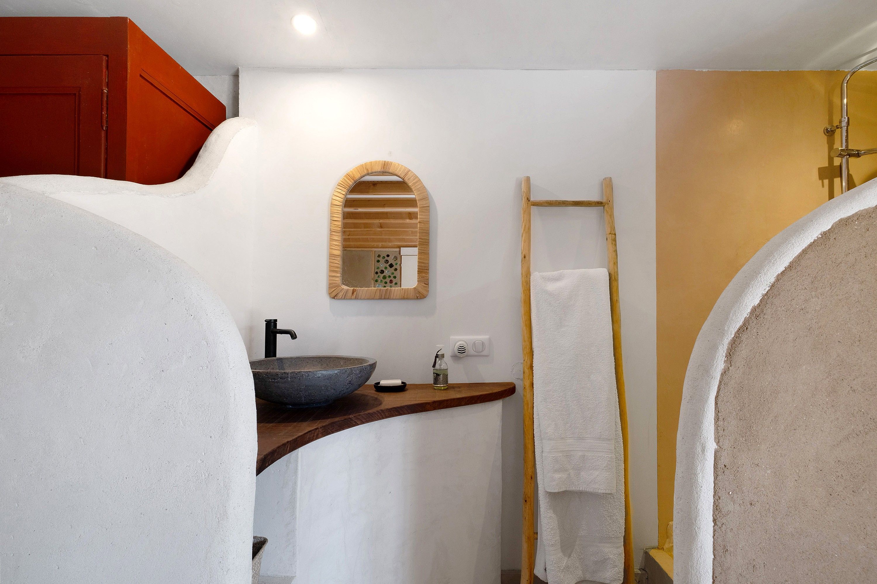 Une salle de bain avec un grand miroir, un porte-serviettes en bois et un lavabo en pierre.