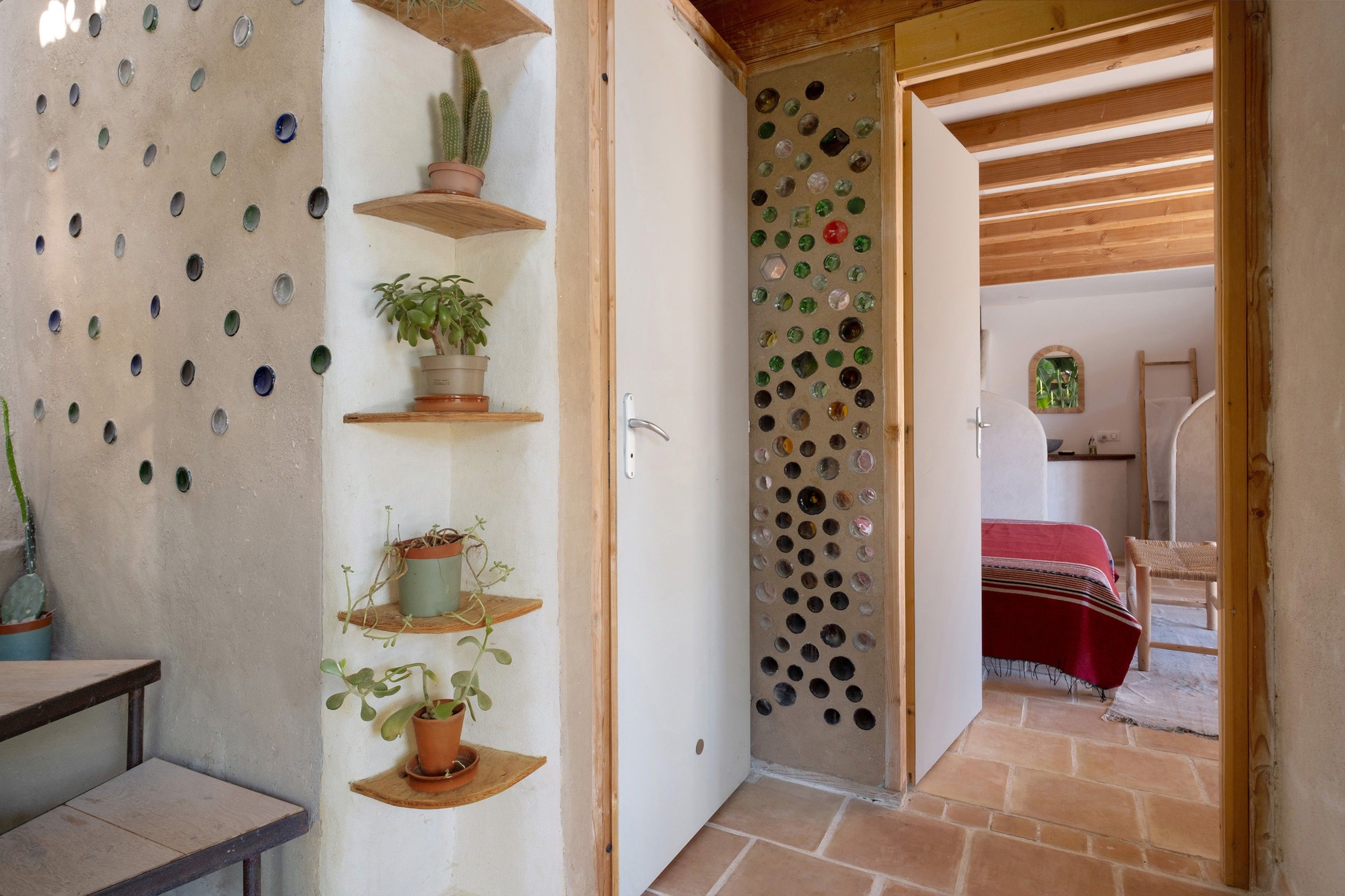 Une pièce avec une porte en bois, un sol carrelé et des étagères ornées de plantes.