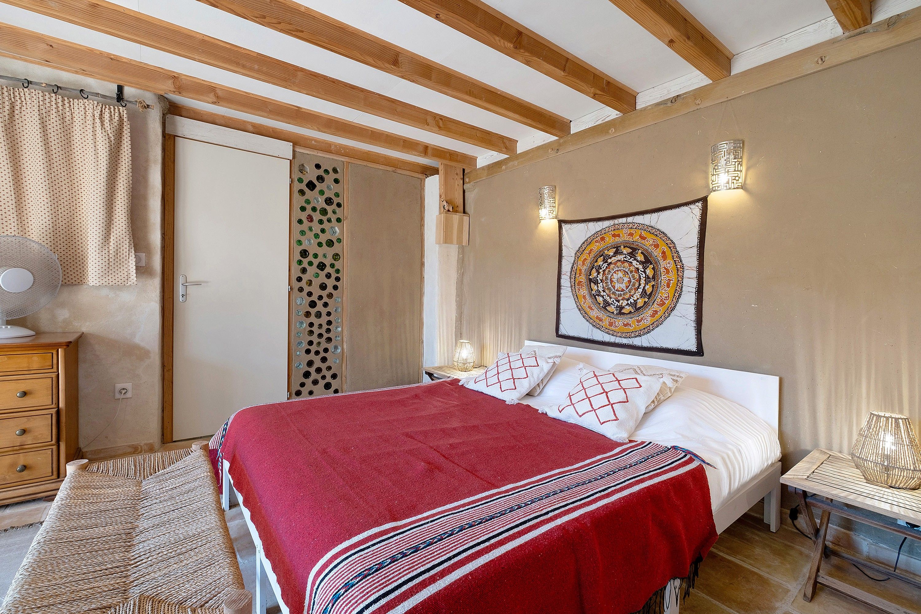 Een slaapkamer met een bed, een houten dressoir, een wandlamp en een wandtapijt.
