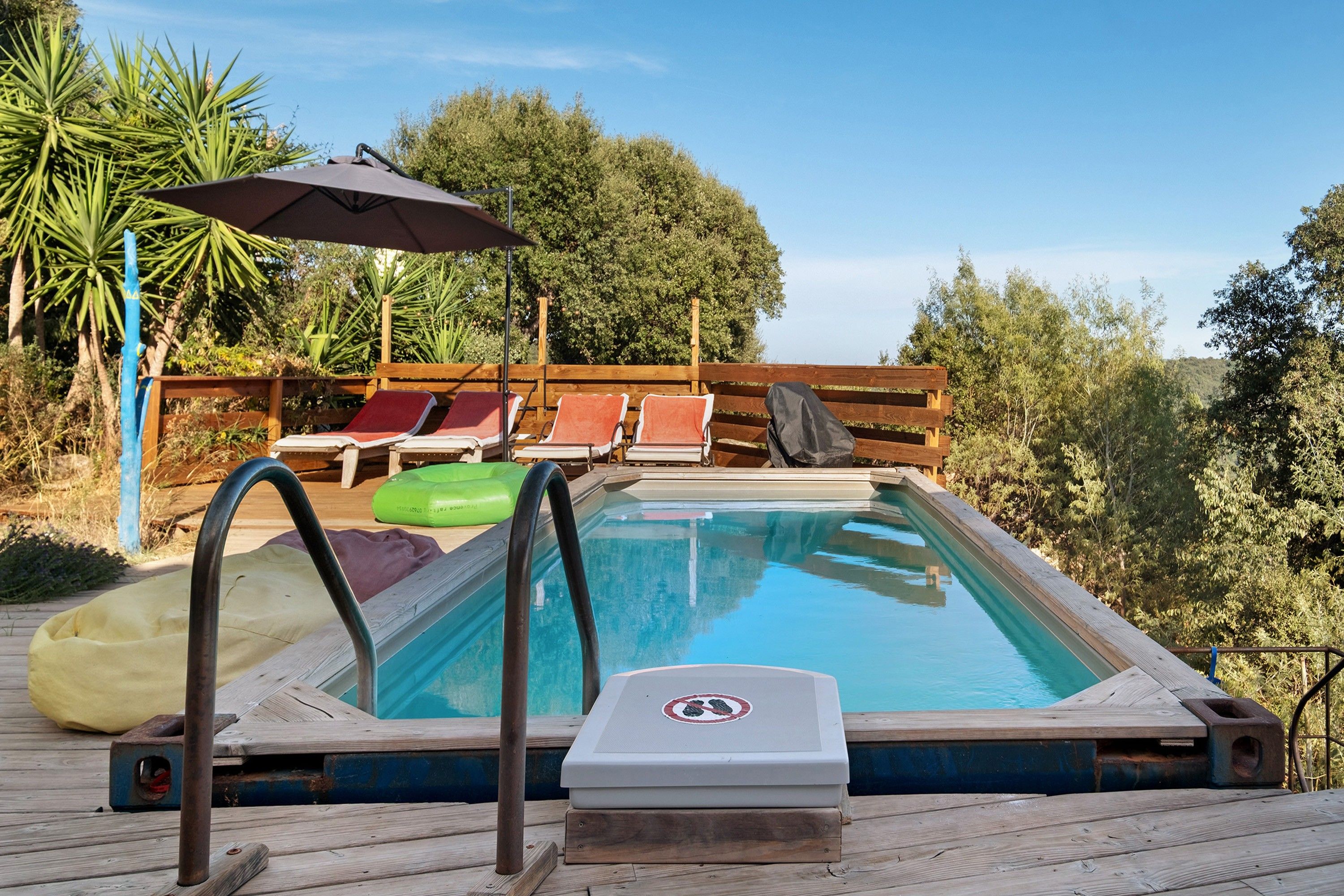 En swimmingpool med træterrasse, liggestole og et overdækket område med parasol.