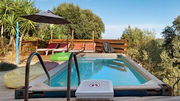 En swimmingpool med træterrasse, liggestole og et overdækket område med parasol.