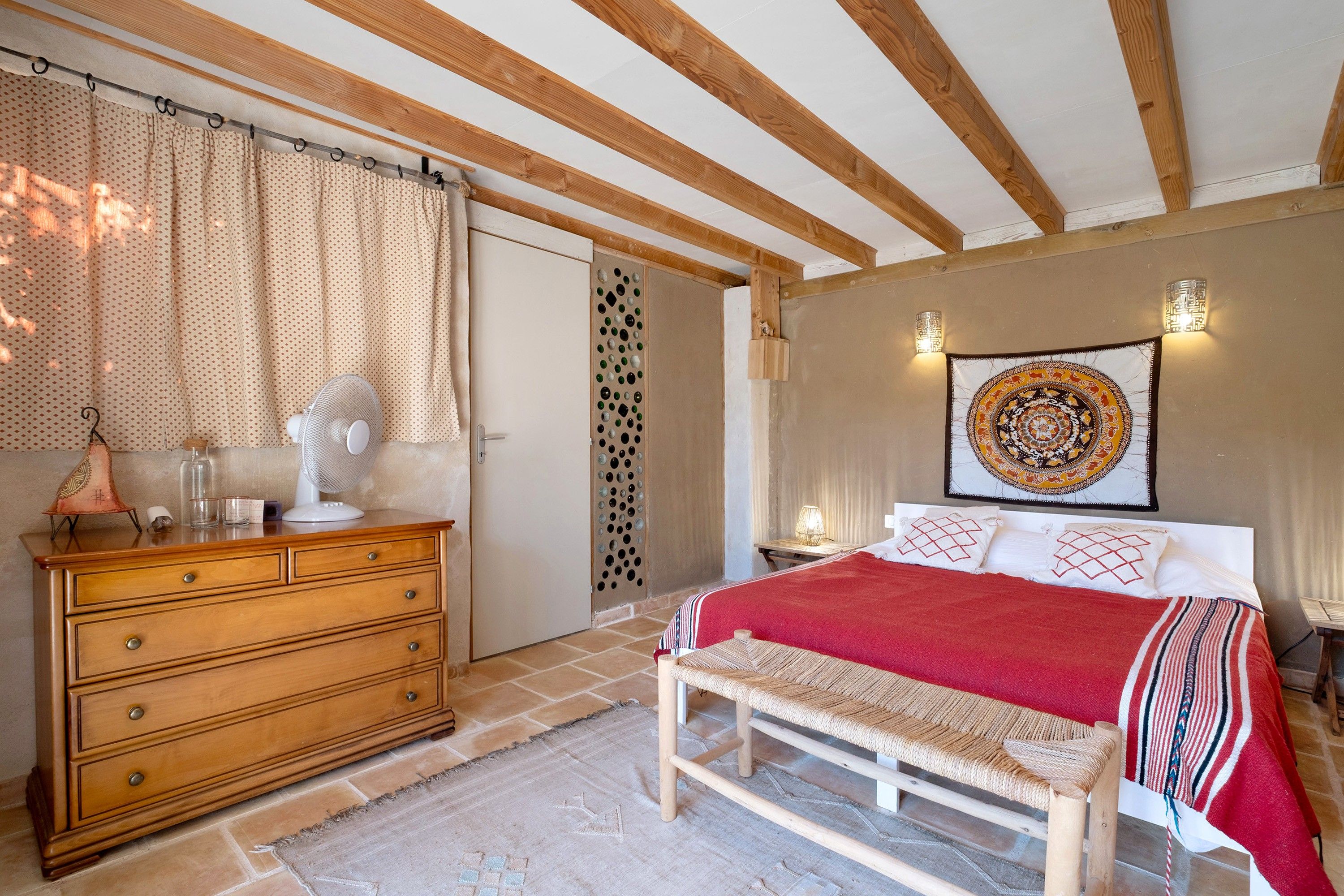 Een slaapkamer met een houten bed, een bankje, een dressoir en een wand met een wandtapijt.
