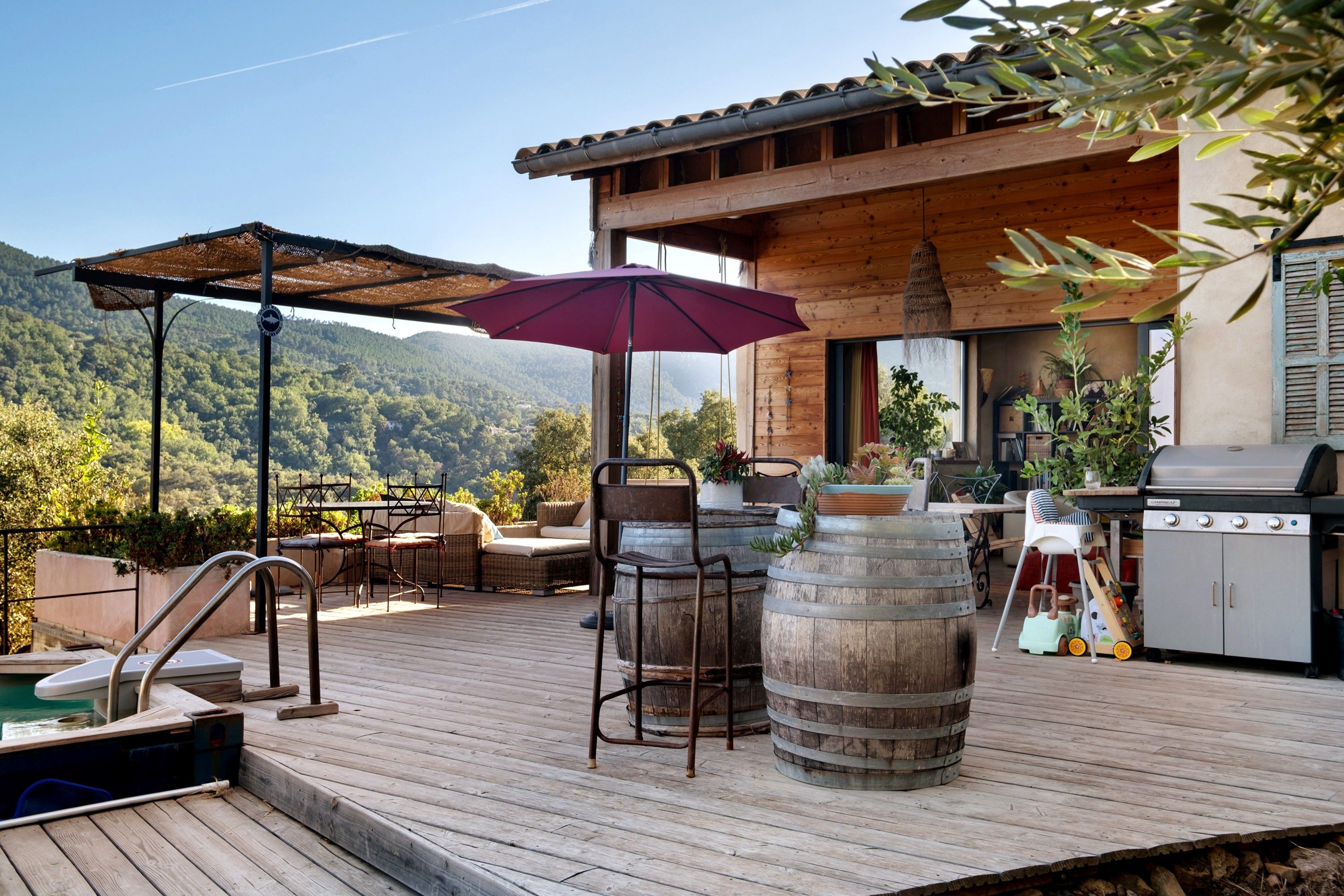 Une terrasse en bois avec des meubles d’extérieur, un barbecue et une vue sur les montagnes.