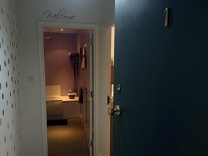A hallway with a 'Welcome' sign, leading to a bathroom with a toilet, sink, and towel rack. - Apartment 3 (Aberdeen)