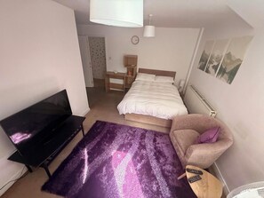 Ein Schlafzimmer mit Bett, Fernseher, Stuhl, Teppich und Heizkörper.
