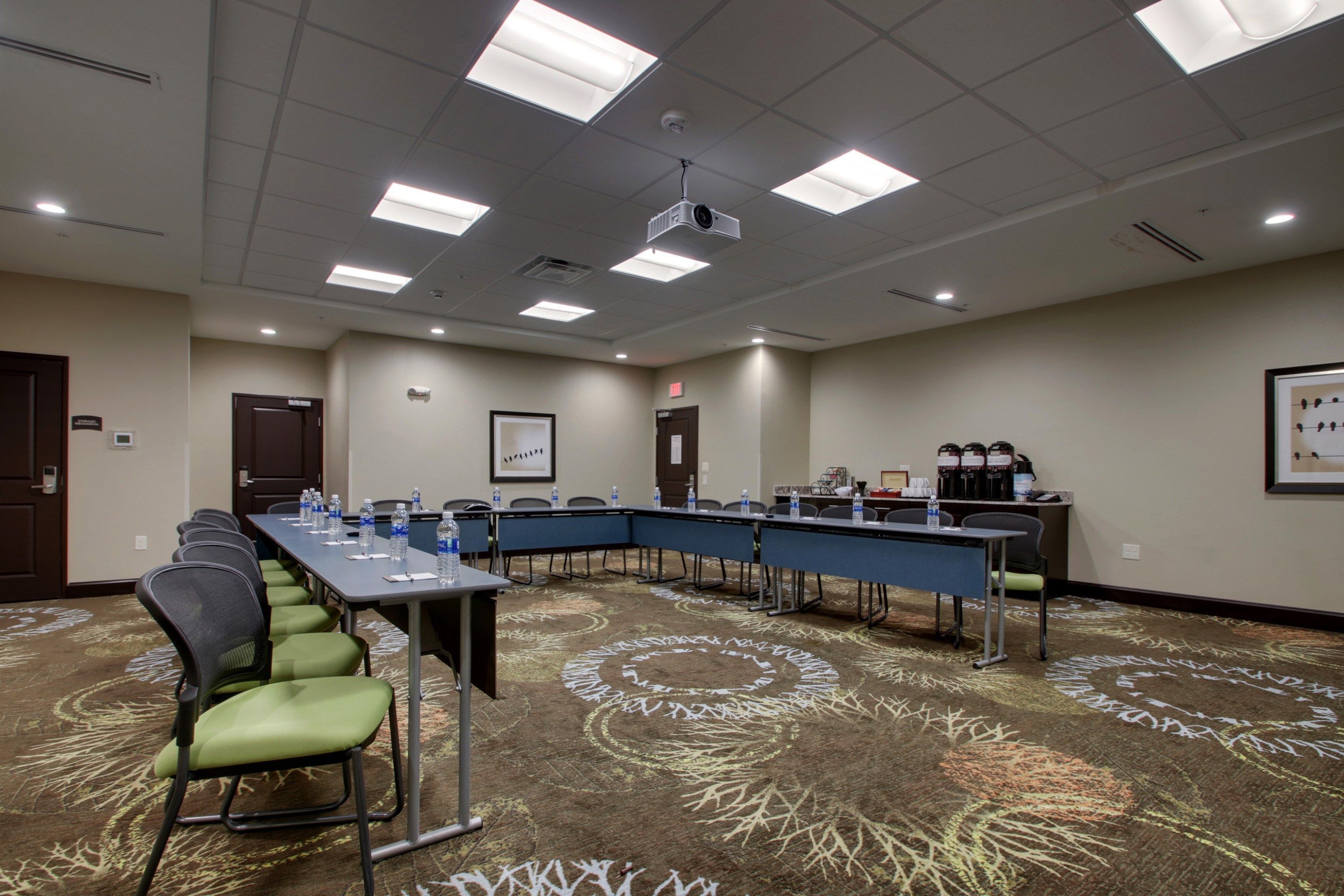 A conference room with a long table, chairs, water bottles, a projector, and a coffee station.
