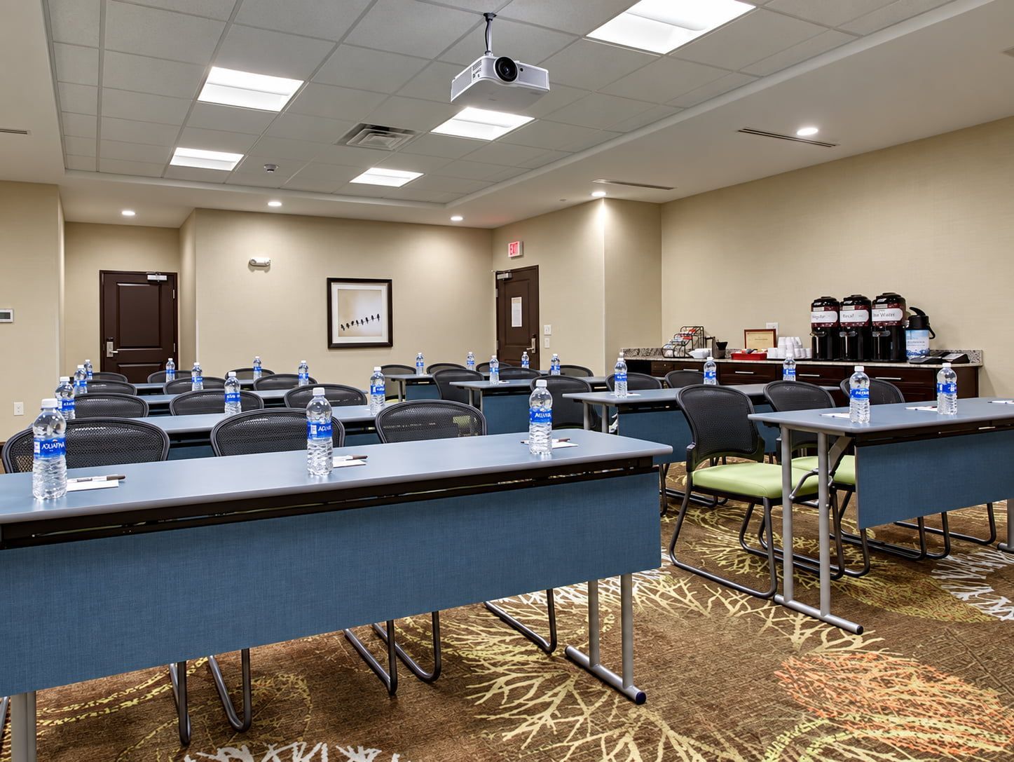 A conference room with tables, chairs, water bottles, a projector, and a coffee station.