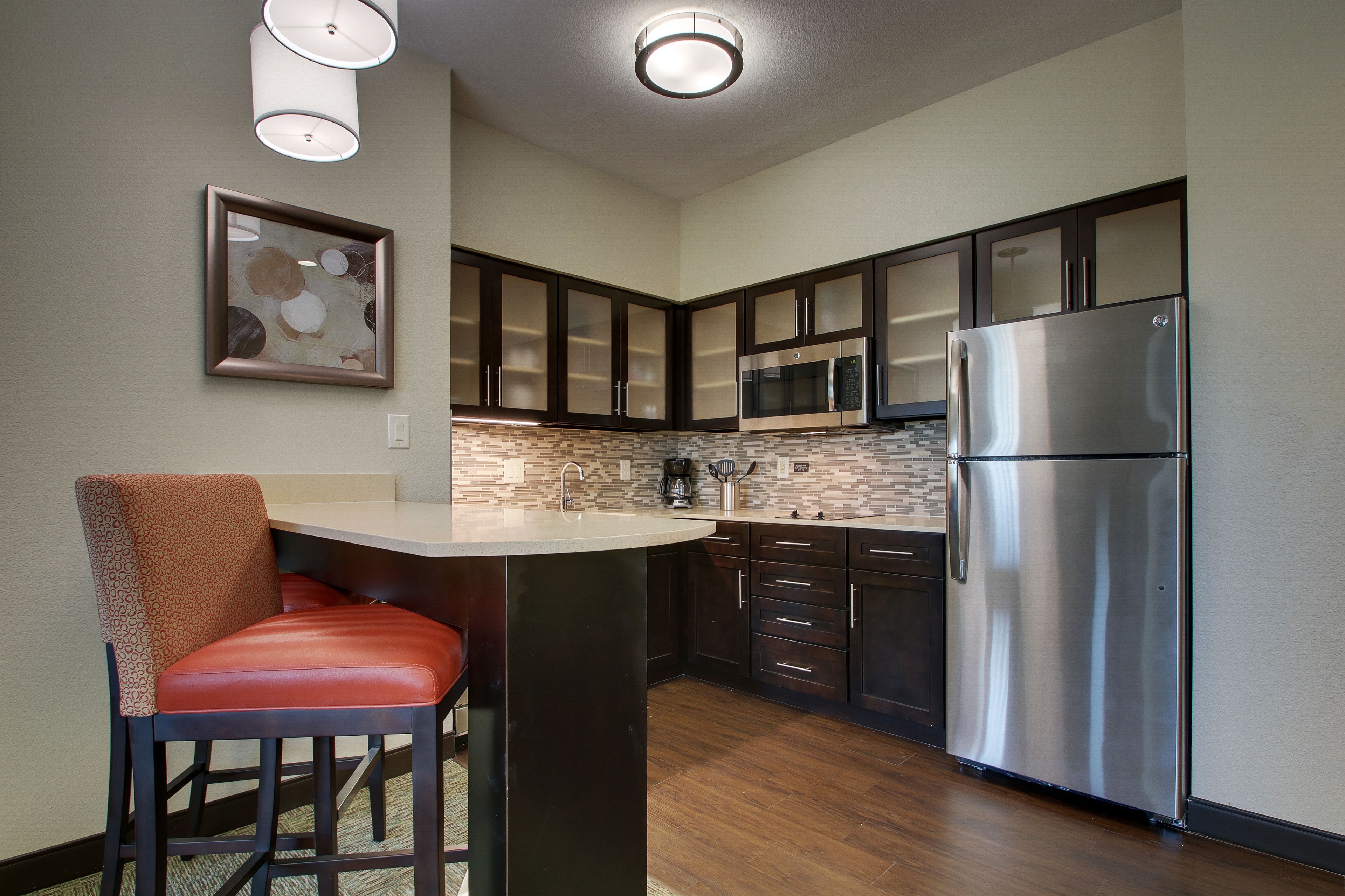 A modern kitchen with dark cabinetry, a stainless steel refrigerator, and a bar stool.