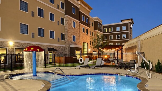 A hotel pool area with a water feature and lounge chairs. - Hearing Accessible King Suite | Free Breakfast! (The Colony)