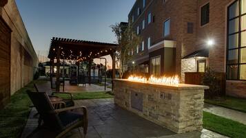 An outdoor patio with a stone fire feature, seating, and a covered area with string lights.