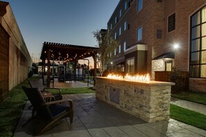An outdoor patio with a stone fire feature, seating, and a covered area with string lights. - ADA King Studio w/ Roll-In Shower | Free Breakfast (The Colony)