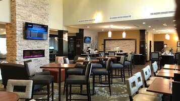 A hotel lobby with multiple seating areas, a fireplace, a TV screen, and a reception desk.