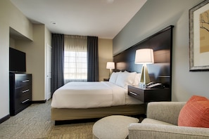 A hotel room with a large bed, bedside lamps, a desk with a telephone, a television, and a framed picture on the wall. - ADA King Studio w/ Roll-In Shower | Free Breakfast (The Colony)