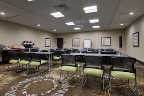 A conference room with tables and chairs, water bottles, framed pictures, and a projector on the ceiling.