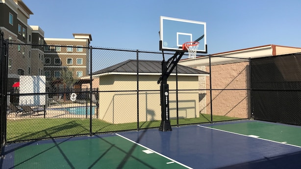 Een buitenbasketbalveld met een hek van gaas, een basketbalring en een zwembad op de achtergrond.