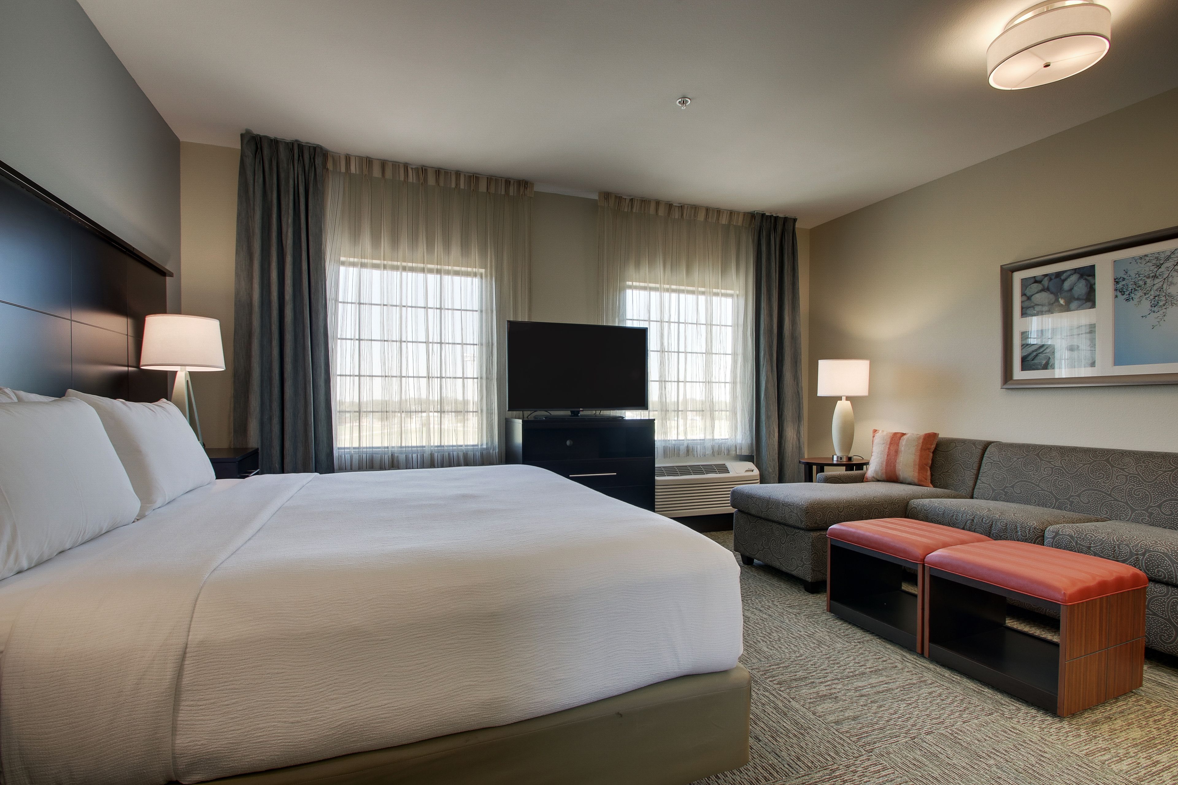 A hotel room with a large bed, a TV, a sofa, and a small table.