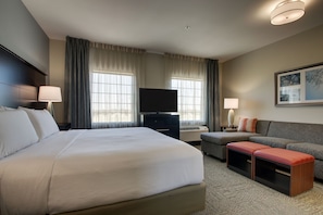 A hotel room with a large bed, a TV, a sofa, and a small table.