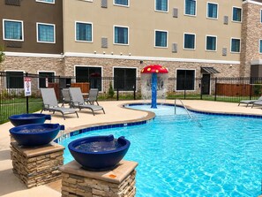 A swimming pool with a water feature, lounge chairs, and a stone facade building in the background.