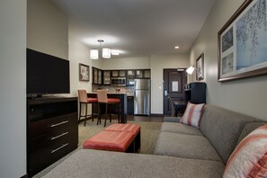 A compact living space with a kitchenette, a sofa with a patterned throw, a flat-screen TV, and a dining area with chairs.