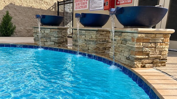 A swimming pool with a stone wall and two large bowls on top. - Large Hearing Accessible Suite | Free Breakfast! (The Colony)