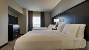 A hotel room with a large bed, a dresser, a television, and a window with curtains. - Large Hearing Accessible Suite | Free Breakfast! (The Colony)