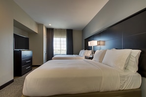 Ein Hotelzimmer mit einem großen Bett, einem Schminktisch, einem Fernseher und einem Fenster mit Vorhängen.