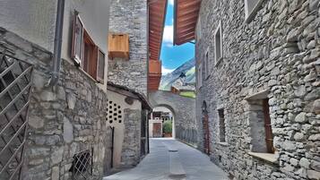 Un étroit sentier pavé de pierres, bordé de bâtiments aux volets en bois et d’un mur de pierres.