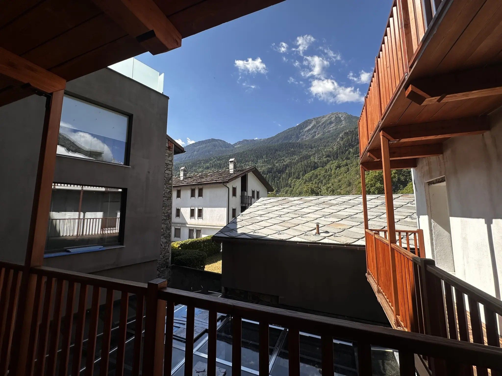 Une vue depuis un balcon, avec une chaîne de montagnes en arrière-plan, mettant en évidence un bâtiment doté d’un toit en pente et d’une balustrade en bois.