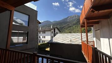 Une vue depuis un balcon, avec une chaîne de montagnes en arrière-plan, mettant en évidence un bâtiment doté d’un toit en pente et d’une balustrade en bois.