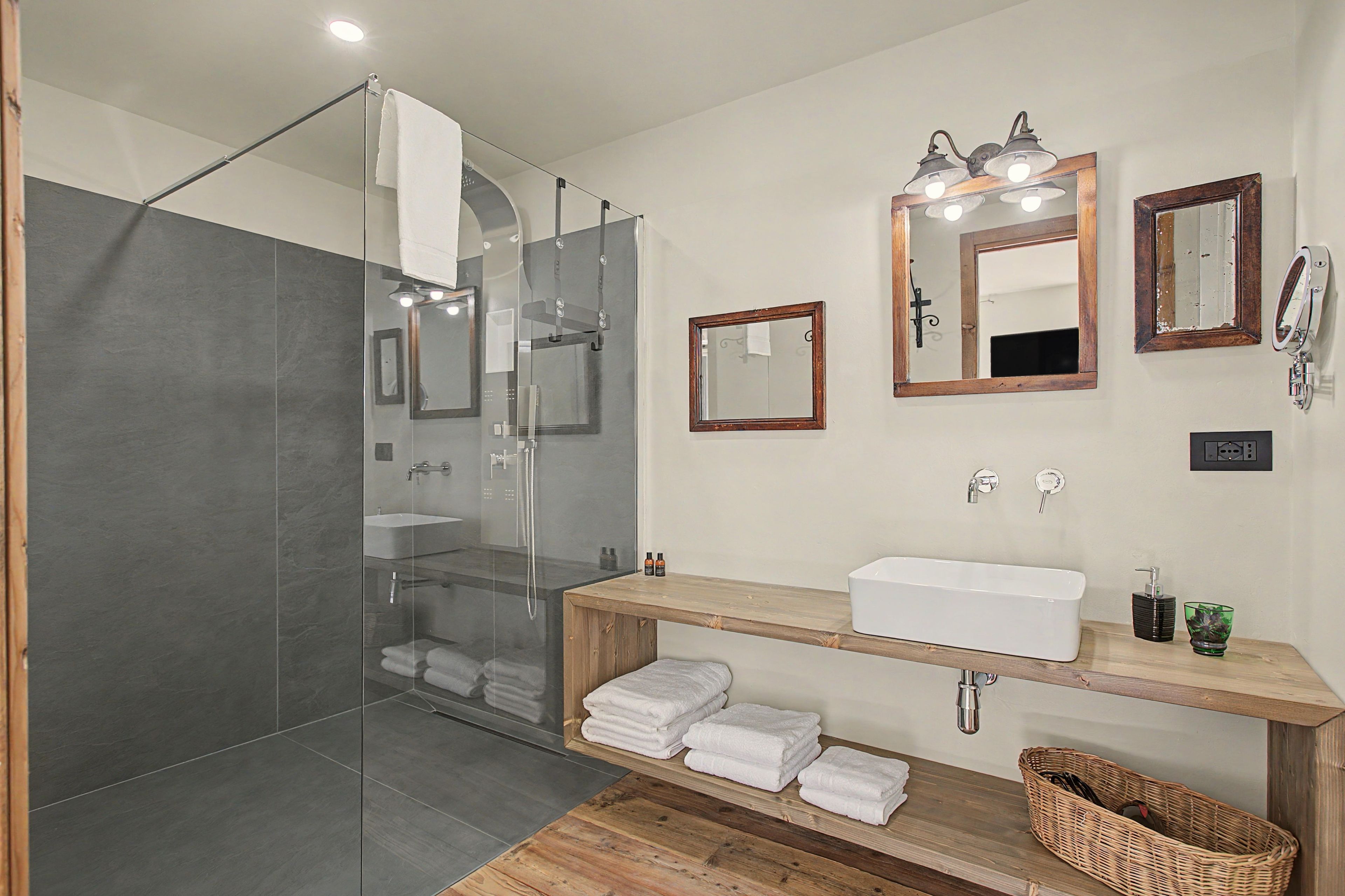 Ein modernes Badezimmer mit einer in Glas abgeschlossenen Dusche, einem Holzbadezimmer-Möbelstück mit Waschbecken und zwei Spiegeln.