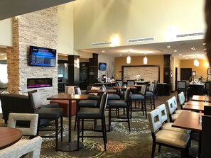 Eine Hotelhalle mit mehreren Sitzbereichen, einem Kamin, einem Fernsehbildschirm und einer Rezeption.