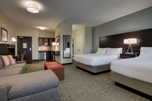 A hotel room with two beds, a sofa, a small table, and a kitchenette.