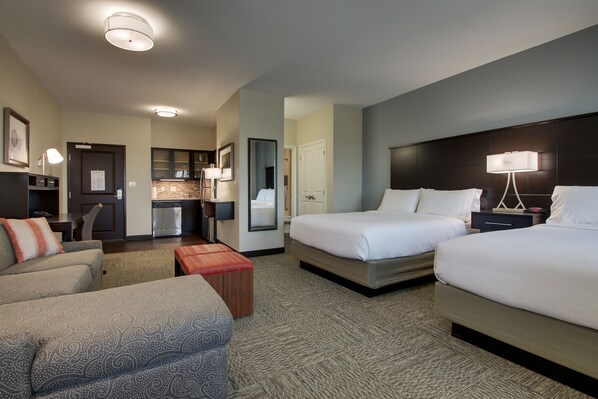 A hotel room with two beds, a sofa, a small table, and a kitchenette.