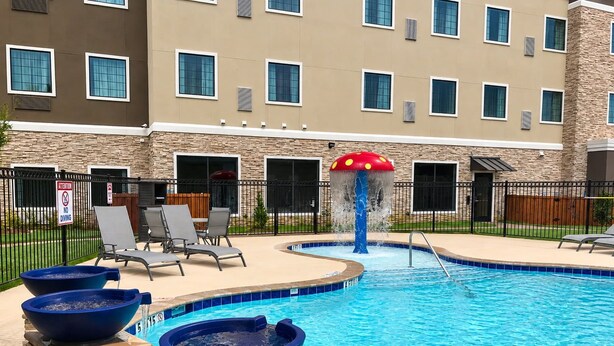 A swimming pool with a water feature, lounge chairs, and a stone facade building in the background. - Studio Suite w/ Kitchen | Daily Breakfast Included (The Colony)