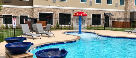 A swimming pool with a water feature, lounge chairs, and a stone facade building in the background.