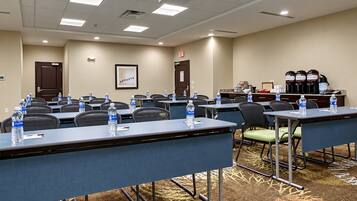 A conference room with tables, chairs, water bottles, a projector, and a coffee station.