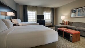 A hotel room with two beds, a television, a sofa, and a small table. - Studio Suite w/ Kitchen | Daily Breakfast Included (The Colony)