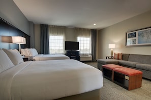 Ein Hotelzimmer mit zwei Betten, einem Fernseher, einem Sofa und einem kleinen Tisch.