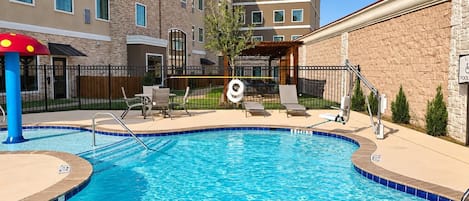 A swimming pool with a lifeguard chair, lounge chairs, and a covered seating area.