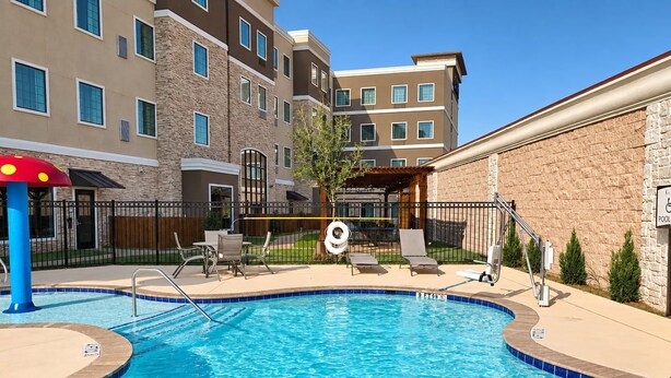 A swimming pool with a lifeguard chair, lounge chairs, and a covered seating area. - King Studio Suite w/ Kitchen | Free Breakfast! (The Colony)