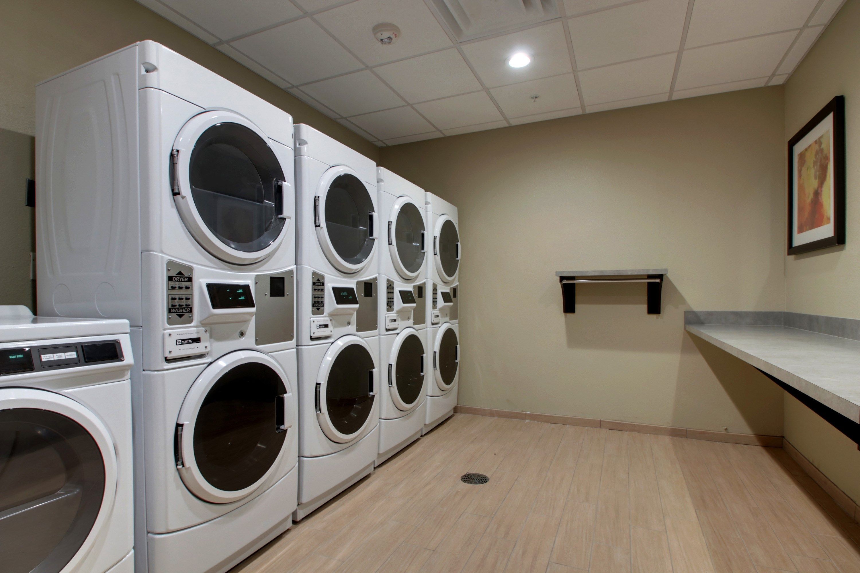 A laundry room with multiple stacked front-loading washing machines, a small shelf, and a tiled floor.