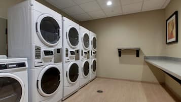 A laundry room with multiple stacked front-loading washing machines, a small shelf, and a tiled floor.