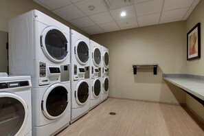 A laundry room with multiple stacked front-loading washing machines, a small shelf, and a tiled floor.