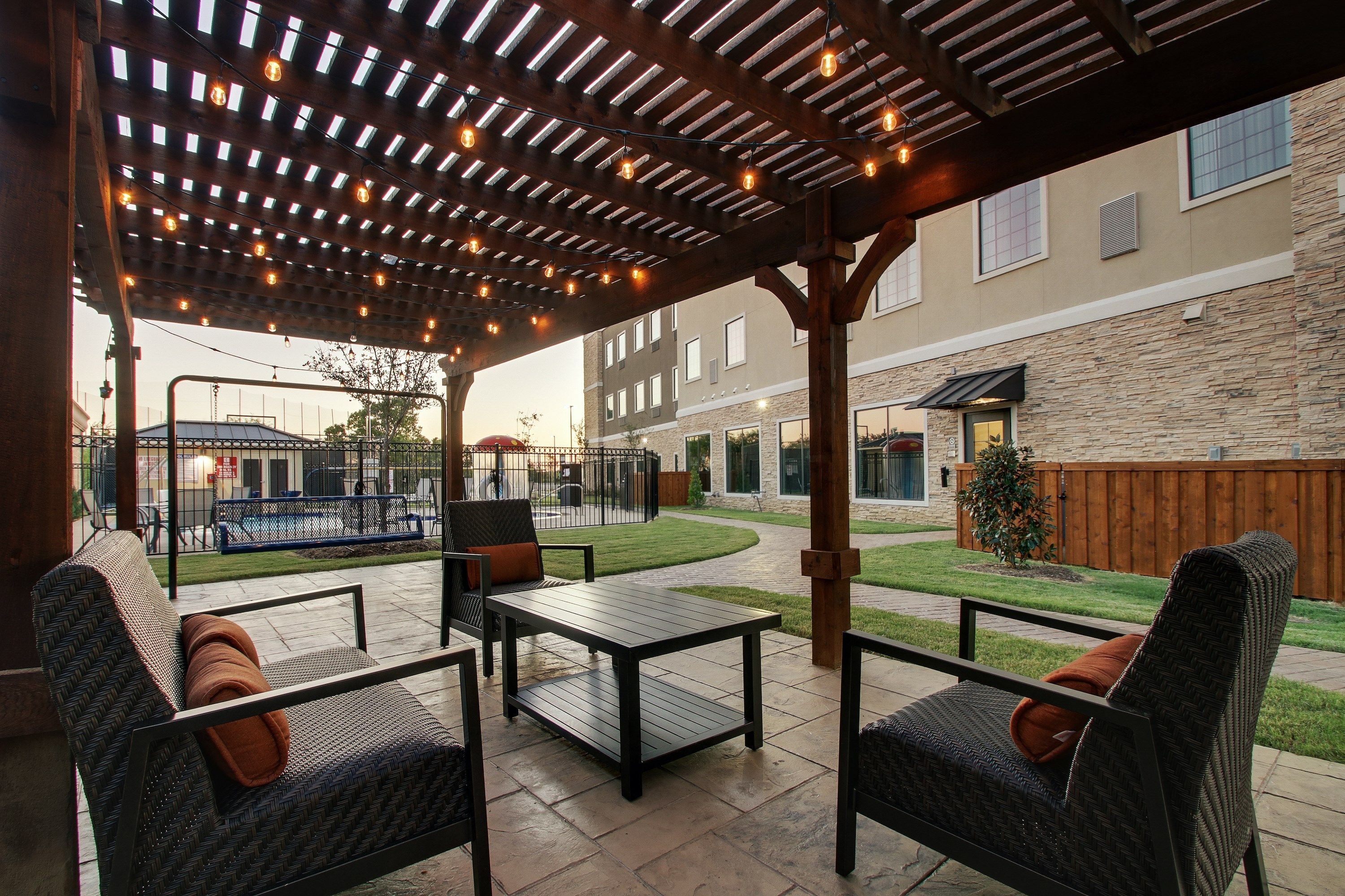 Une terrasse extérieure avec des meubles en osier et une pergola illuminée de guirlandes lumineuses.